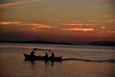 Silhouette people in boat on sea against sky