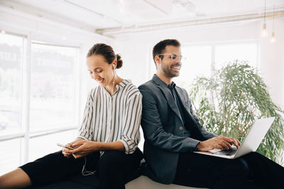 Smiling business coworkers using smart phone and laptop at creative office