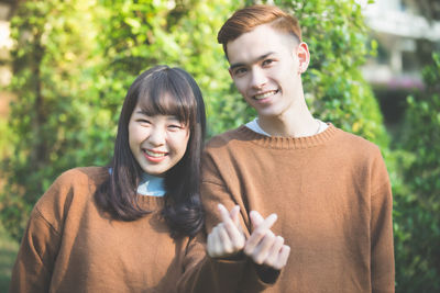 Portrait of smiling young couple gesturing tiny sign against plants
