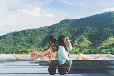 Woman sitting on mountain against sky