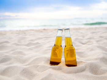 Beer bottle on sand at beach against sky