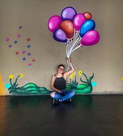 Woman holding colorful balloons against wall