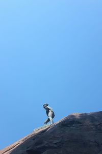 Low angle view of man on rock against clear blue sky