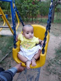 Cropped hand of man by girl sitting on swing