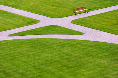 Cobbled park alleys and a wooden park bench. all surrounded by green grass. park seen from above.