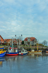 Boats moored in river by buildings against sky