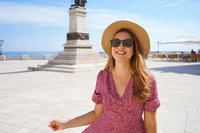 Young woman wearing sunglasses standing against built structure