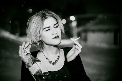 Close-up of young woman smoking cigarette while holding alcohol bottle at night