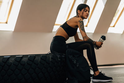 Side view of young woman sitting on tire at gym