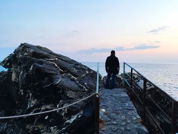 Rear view of silhouette man standing on rock against sea