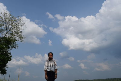 Portrait of young woman standing against cloudy sky