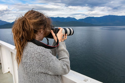 Rear view of woman photographing lake against mountains