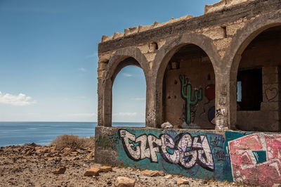 Graffiti on wall by sea against sky