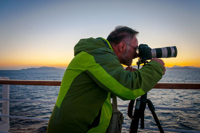 Man taking photographs from the deck of a cruise ship at sunset