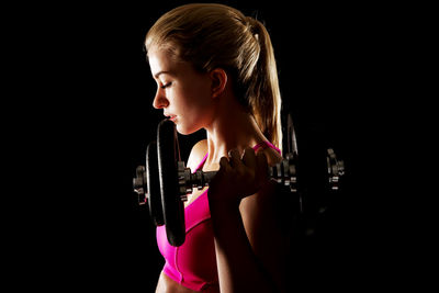 Young woman lifting dumbbell against black background