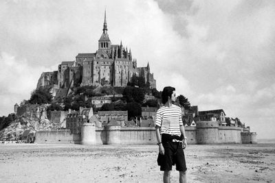 Young man looking away while standing against castle 