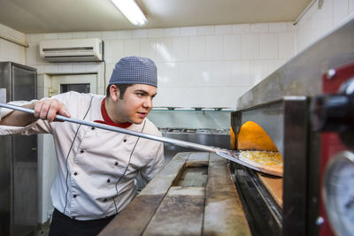 Chef introducing a pizza in a hot oven in a restaurant kitchen.