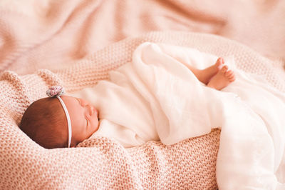 Baby girl with headband sleeping on knitted blanket