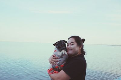 Portrait of woman with dog standing against sea