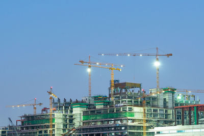 Low angle view of crane at construction site against clear blue sky