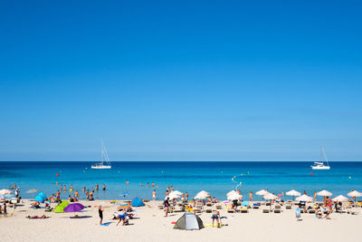 People at beach against clear blue sky