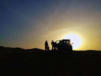 Silhouette men on truck on landscape against sky during sunset