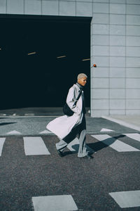 Young woman with hands in pockets crossing road during sunny day