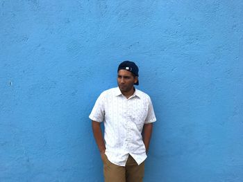 Man with hands in pockets standing against blue wall