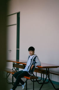 Man sitting on chair by table against wall