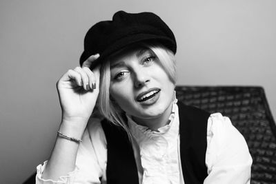 Portrait of young woman wearing hat standing against wall