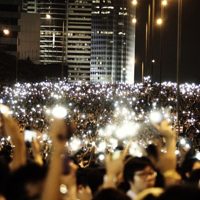 illuminated, night, building exterior, celebration, city, lighting equipment, architecture, built structure, defocused, light - natural phenomenon, crowd, glowing, light, outdoors, large group of people, lens flare, nightlife, firework display, event, selective focus