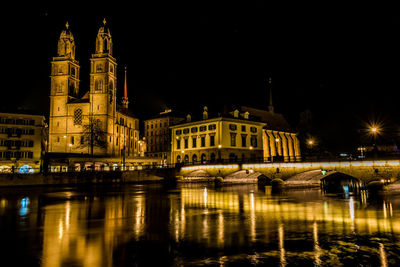 Illuminated buildings by river against sky at night