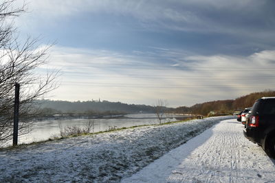 Road on snow covered field against sky