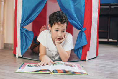 Boy reading book while lying on floor at home