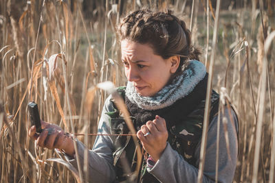 Woman holding mirror compass standing amidst field in forest