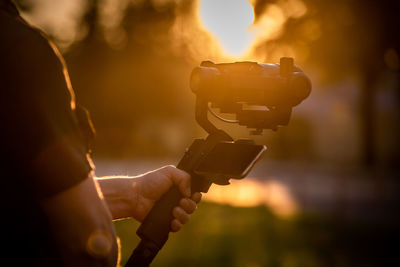 Close-up of man holding camera during sunset