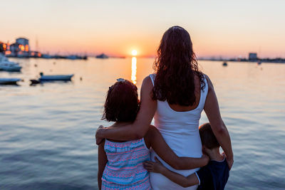 Rear view of women standing at sea during sunset