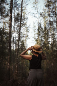 Rear view of woman standing by trees in forest