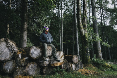 Man sitting on log against trees at forest