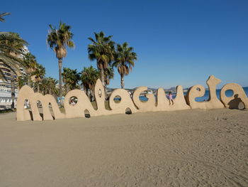 Text on sand at beach against clear blue sky