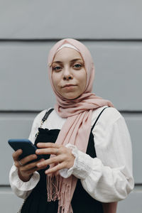 Young woman with smart phone standing in front of wall