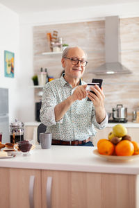 Senior man using mobile phone at kitchen