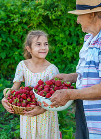 Smiling girl with grandmother holding bowl of strawberries