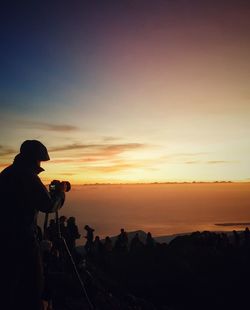 Silhouette man photographing on landscape against sky during sunset