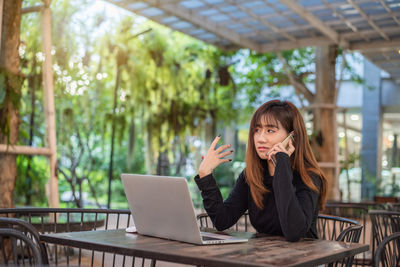 Young woman using phone while sitting on table