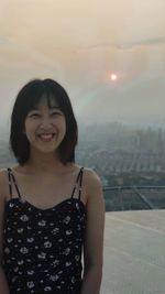 Portrait of smiling woman standing in city against sky