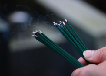 Cropped hands of person holding burning incense sticks