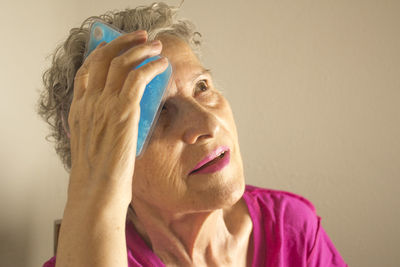 Close-up of woman holding ice pack to forehead against brown background