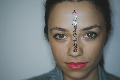 Portrait of beautiful young woman with sequins on face against wall