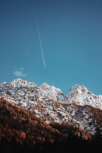 Low angle view of snowcapped mountains against blue sky